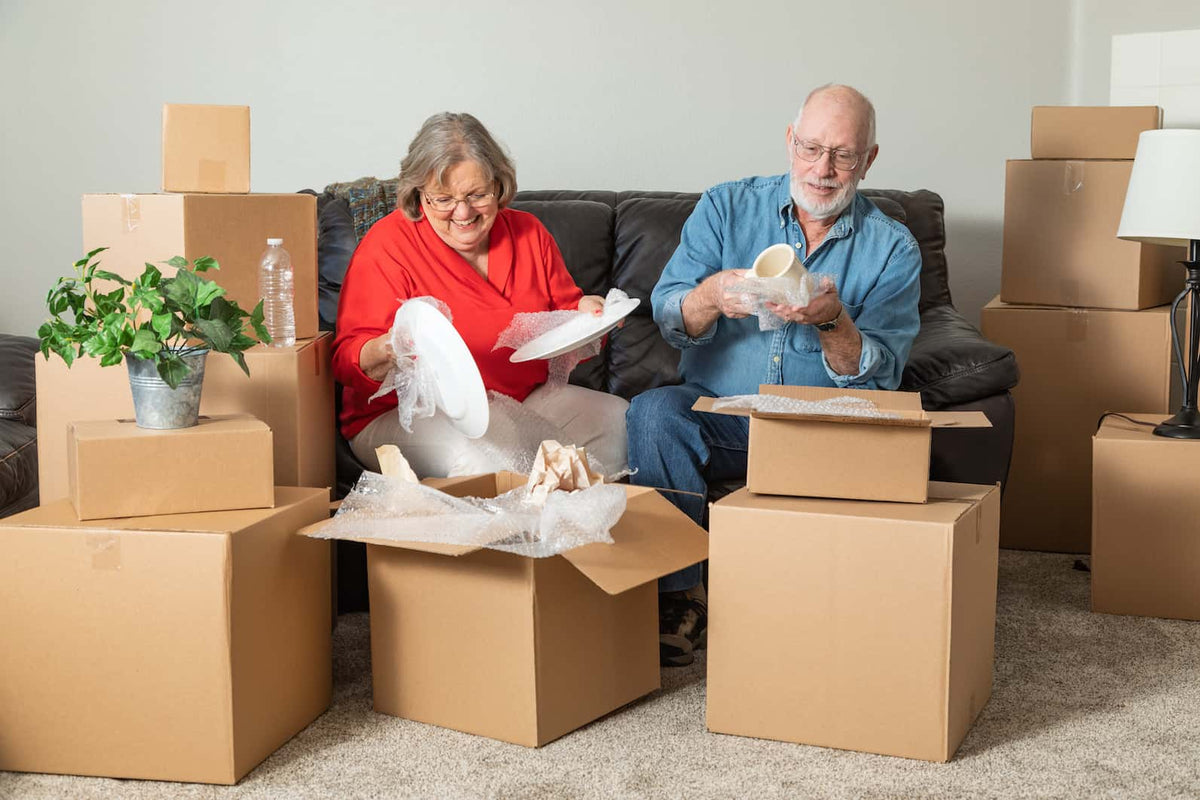 An older couple carefully packing dishes among moving boxes