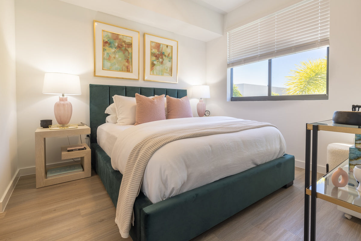 Finished bedroom with a teal upholstered bed, bedside lamps and framed artwork.