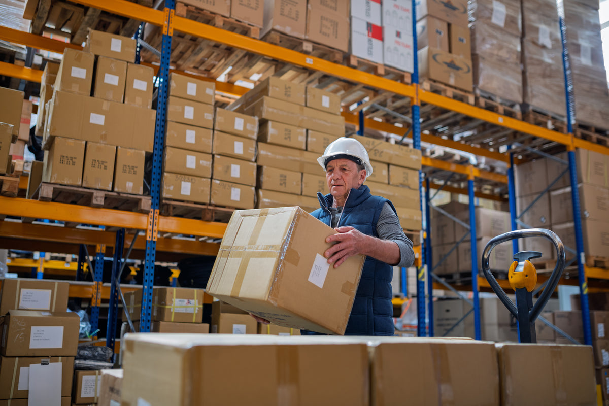 A warehouse worker checking a boxed delivery among storage racks