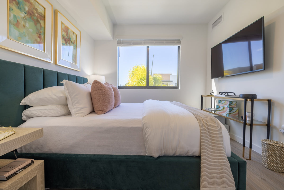 Another view of the furnished bedroom, with the teal bed and a slim console along the opposite wall.