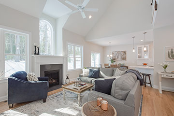 The furnished living room with a sofa, blue armchair, patterned rug, tables and artwork.